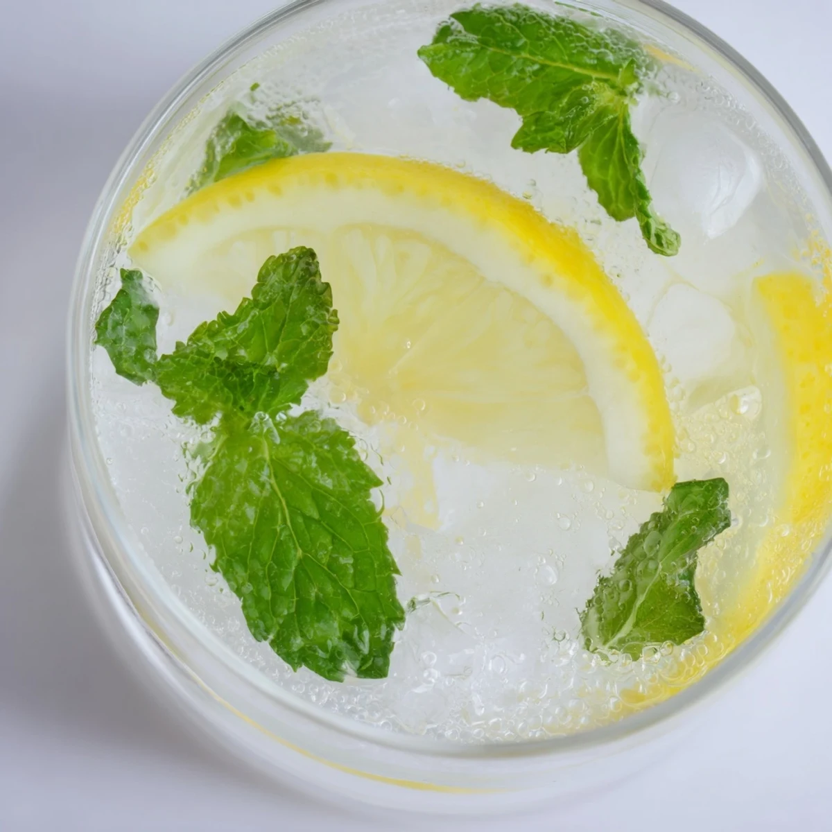 A clear glass of homemade lemon water, garnished with fresh mint, ready to drink.