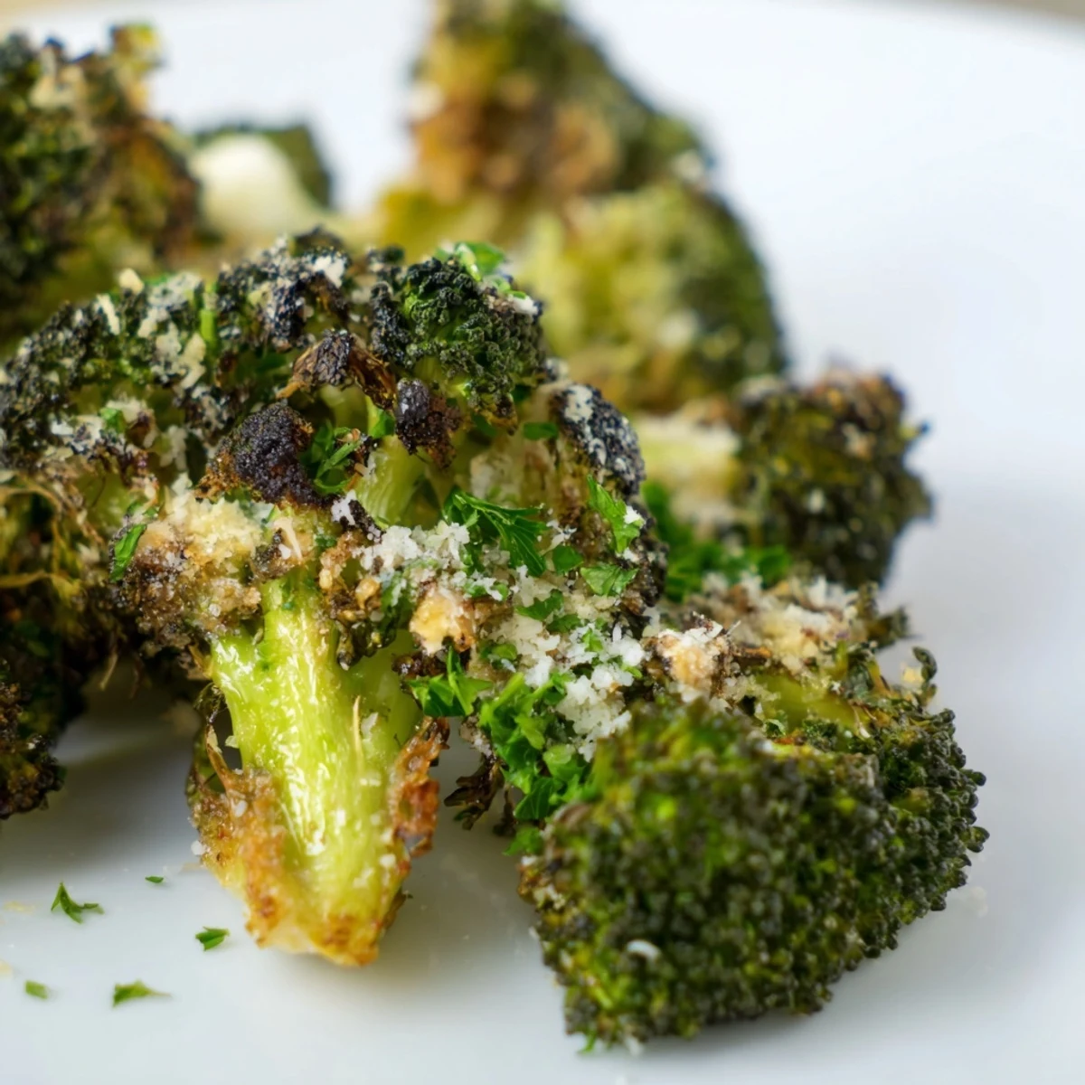 Close-up of roasted broccoli with garlic and Parmesan cheese garnished with fresh parsley and lemon wedges for brightness.