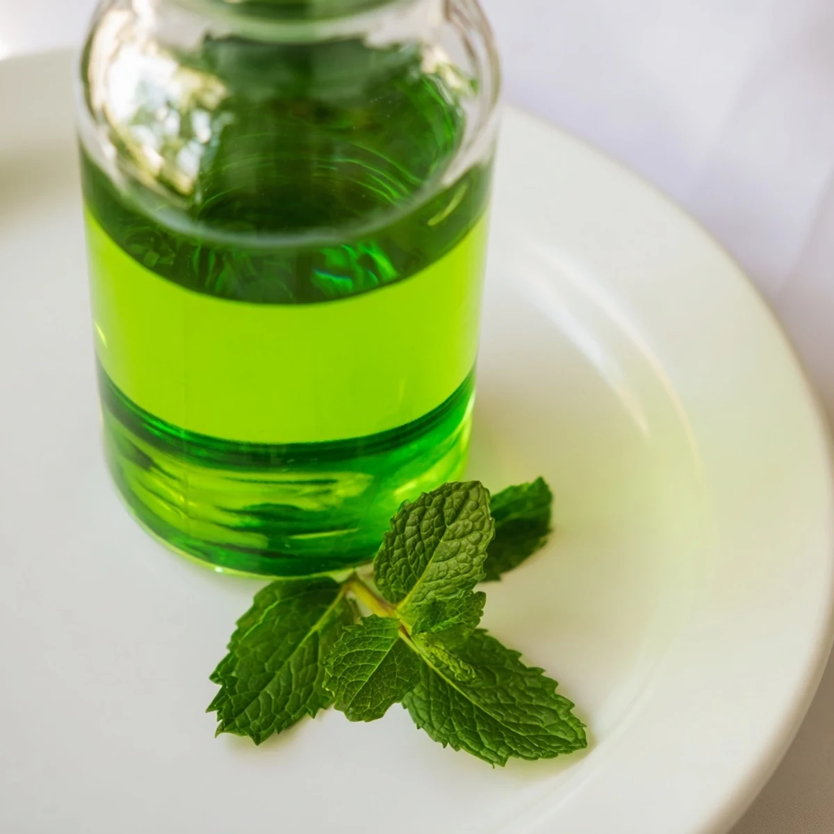 Homemade peppermint extract steeping in a glass jar with fresh leaves and glycerin.