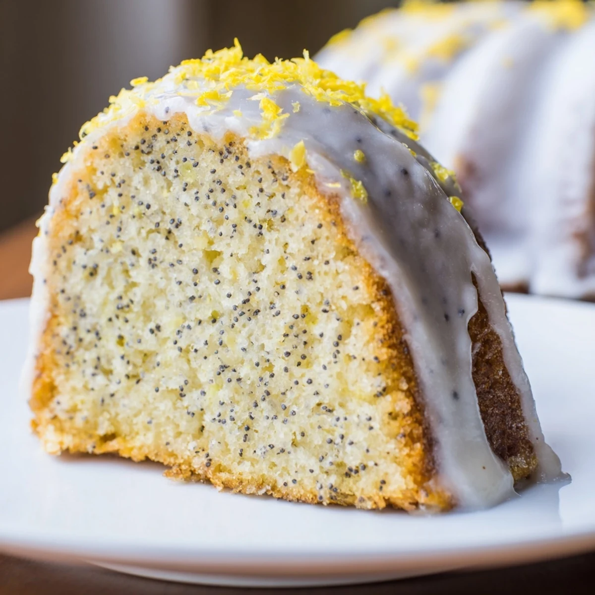 Drizzled Lemon Poppy Seed Bundt Cake with Lemon Cream Glaze on a white plate, garnished with fresh lemon slices and a sprig of mint.