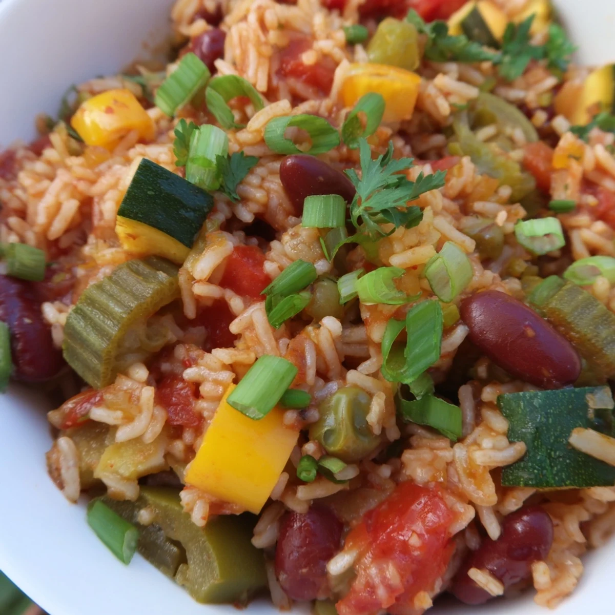 A close-up of Mardi Gras Veggie Jambalaya in a skillet, showing colorful diced bell peppers, okra, and kidney beans mixed with fluffy rice.