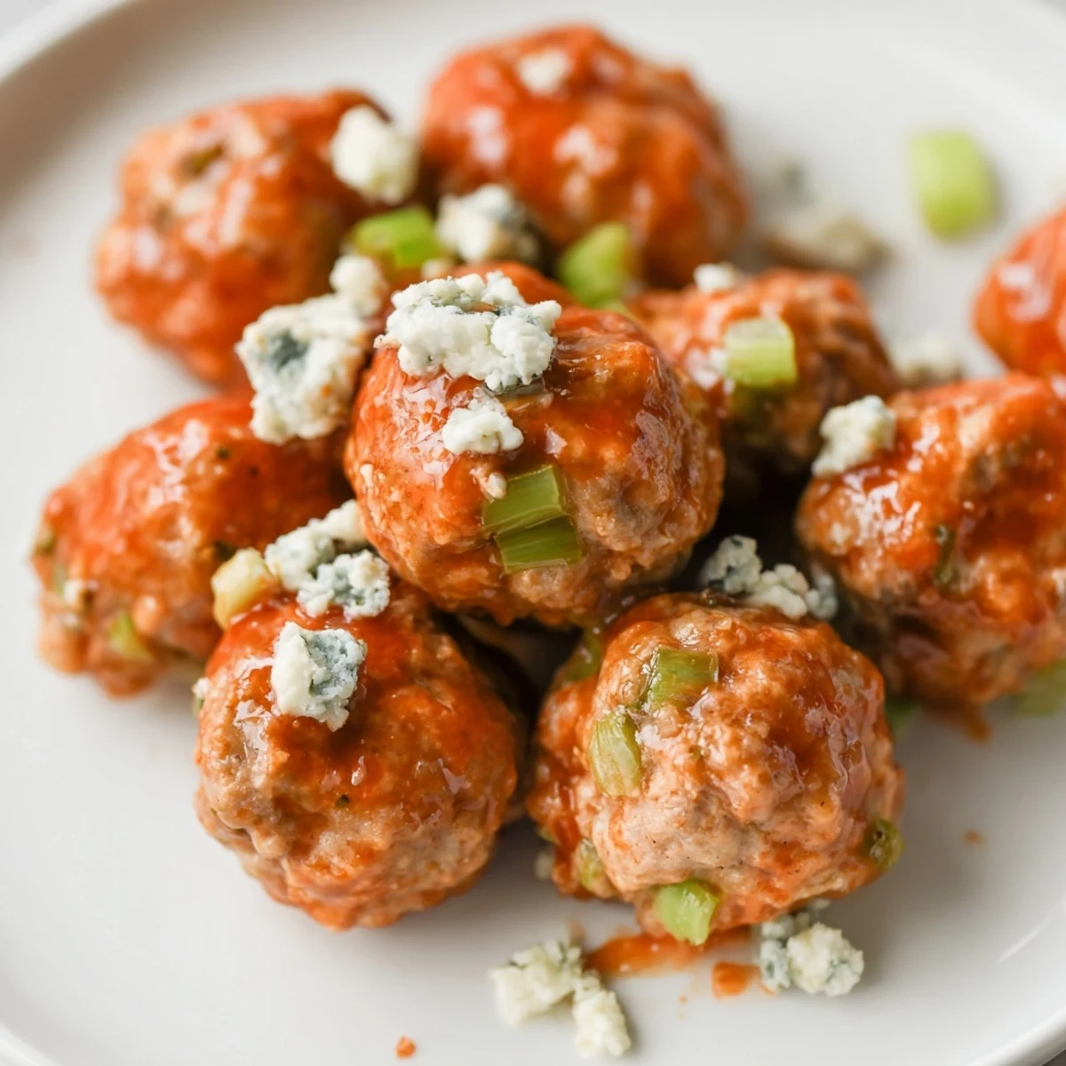Touchdown Buffalo Chicken Meatballs coated in a glossy, spicy red sauce are arranged on a platter with crisp celery and carrot sticks.