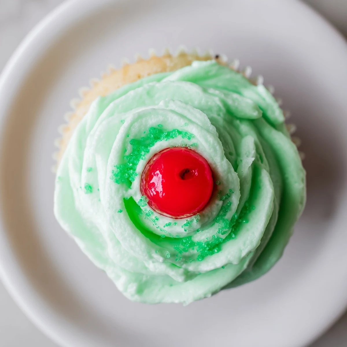 A close-up of moist, green cupcakes with swirls of creamy mint frosting and a maraschino cherry on top.