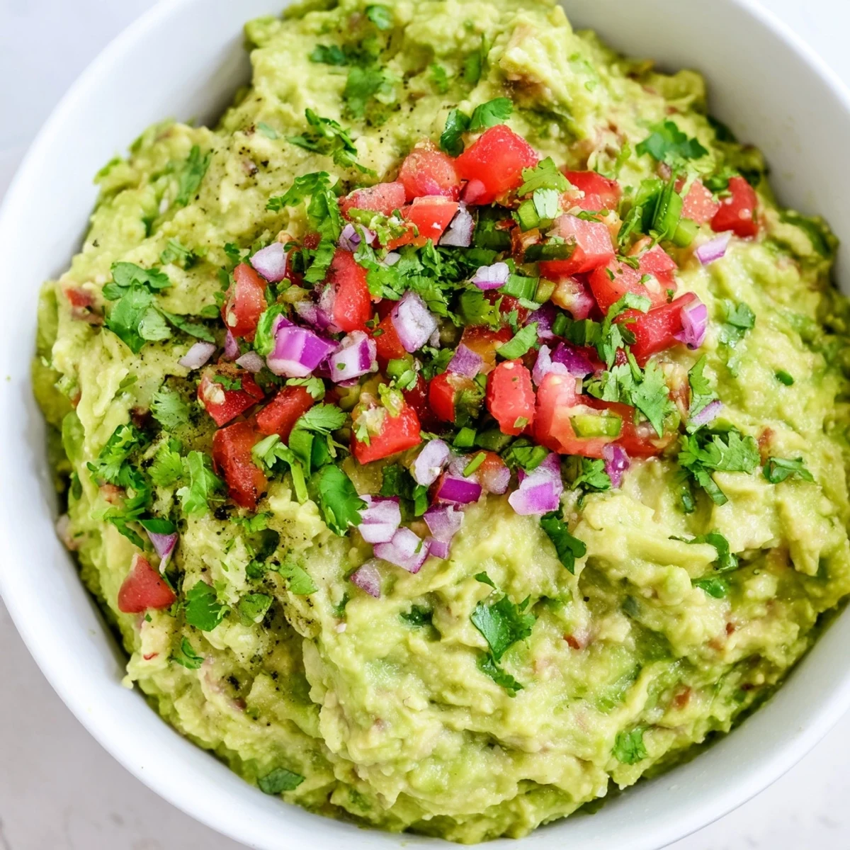 A bright serving bowl of Super Bowl Guacamole with Pico de Gallo, topped with fresh pico and lime wedges next to crispy tortilla chips.