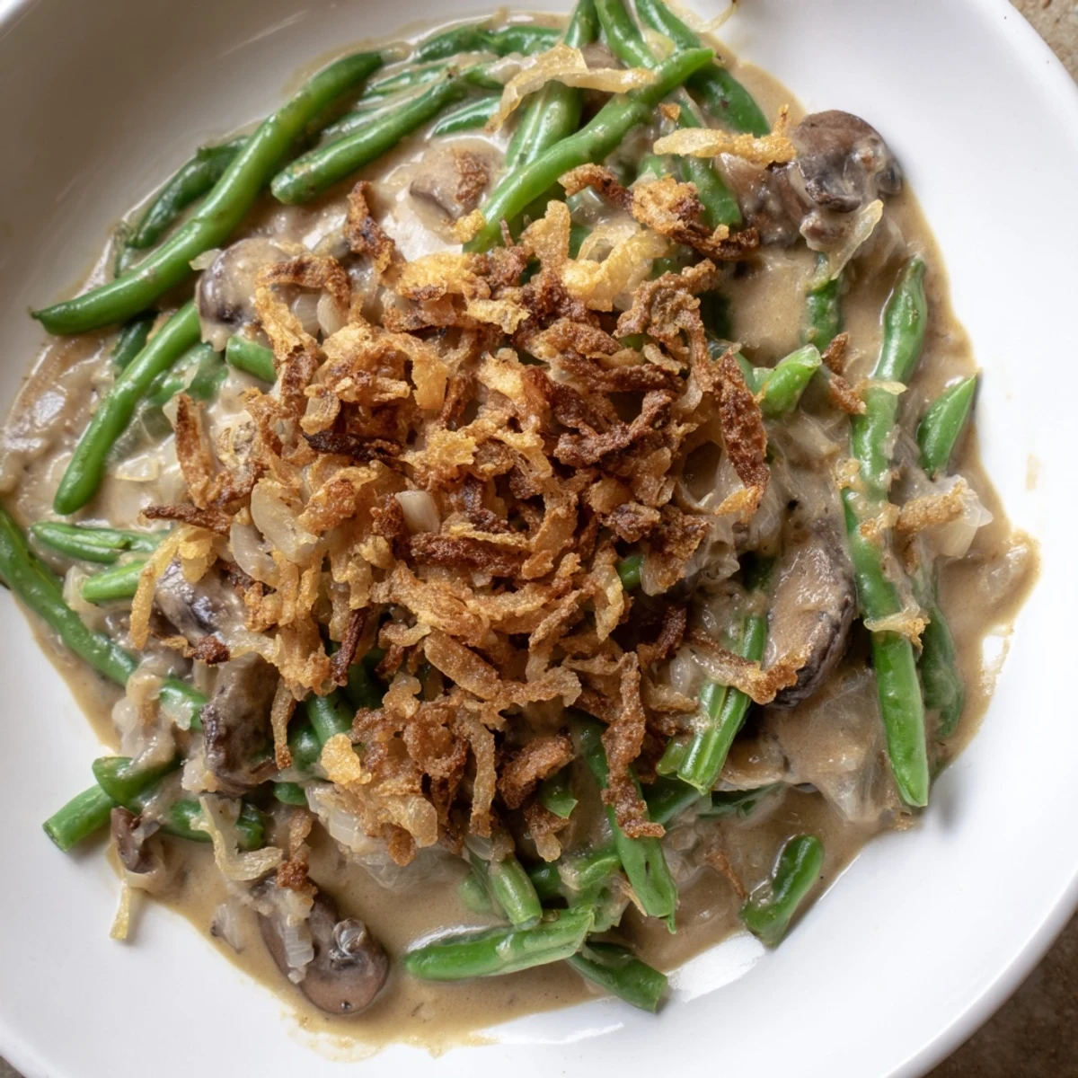 A spoon lifts a serving of Green Bean Casserole, showcasing the creamy sauce and crunchy topping.