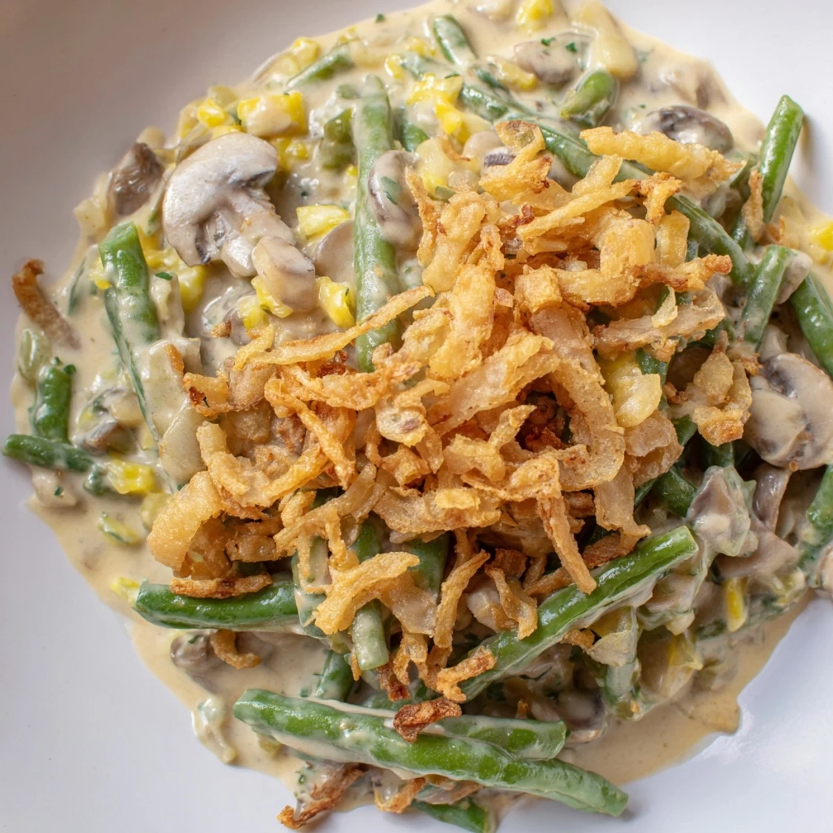 In a white baking dish, Green Bean Casserole with Crispy Onions is served as a warm side, its savory aroma hinting at tender beans and sautéed mushrooms.