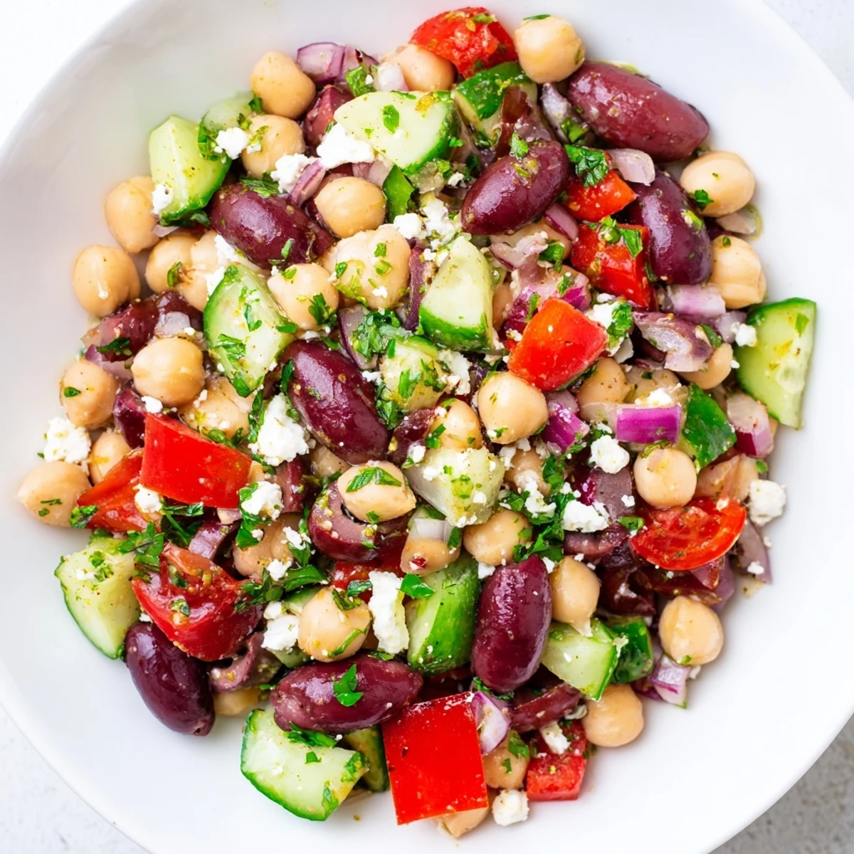 Fresh Mediterranean Dense Bean Salad in a white bowl with chickpeas, tomatoes, cucumber, and crumbled feta cheese.