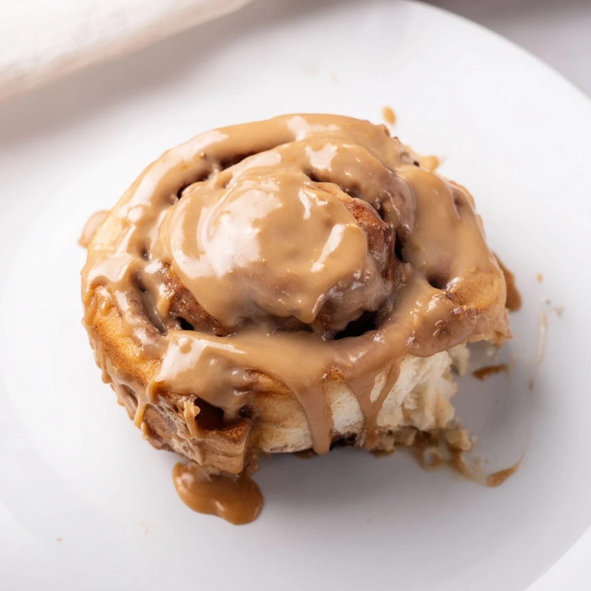 Freshly baked Soft and Gooey Biscoff Cinnamon Rolls are served on a white plate next to a steaming cup of coffee.