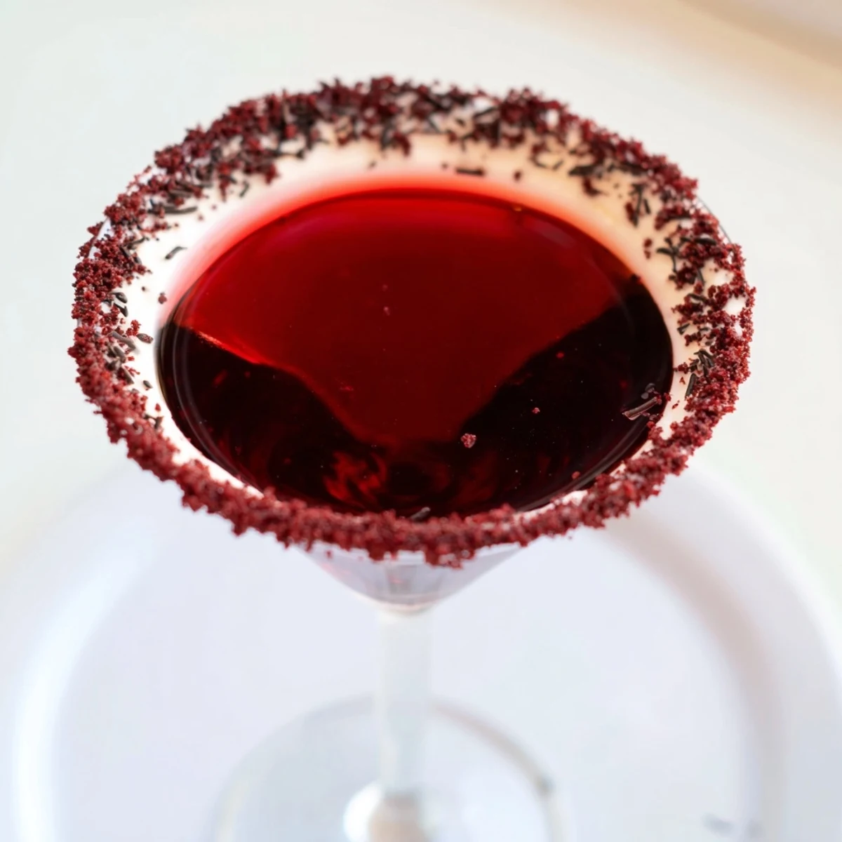 Chilled Decadent Red Velvet Martini in a glass rimmed with cream cheese frosting and chocolate shavings.