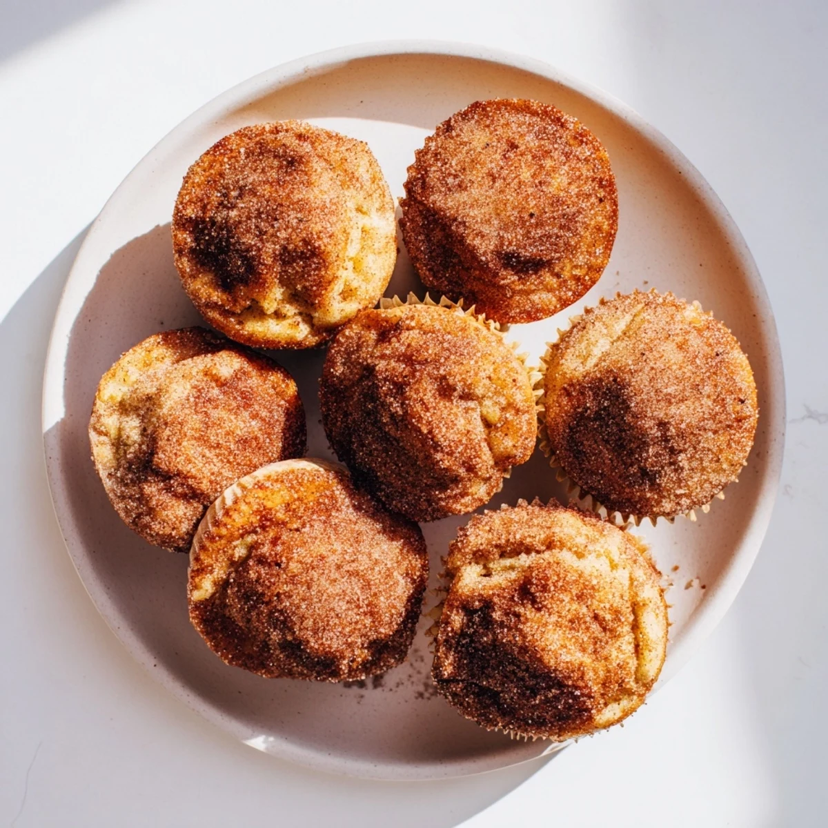 Freshly baked Cinnamon Sugar French Toast Muffins are showcased on a cooling rack, their cinnamon-sugar coating glistening under bright kitchen lighting.