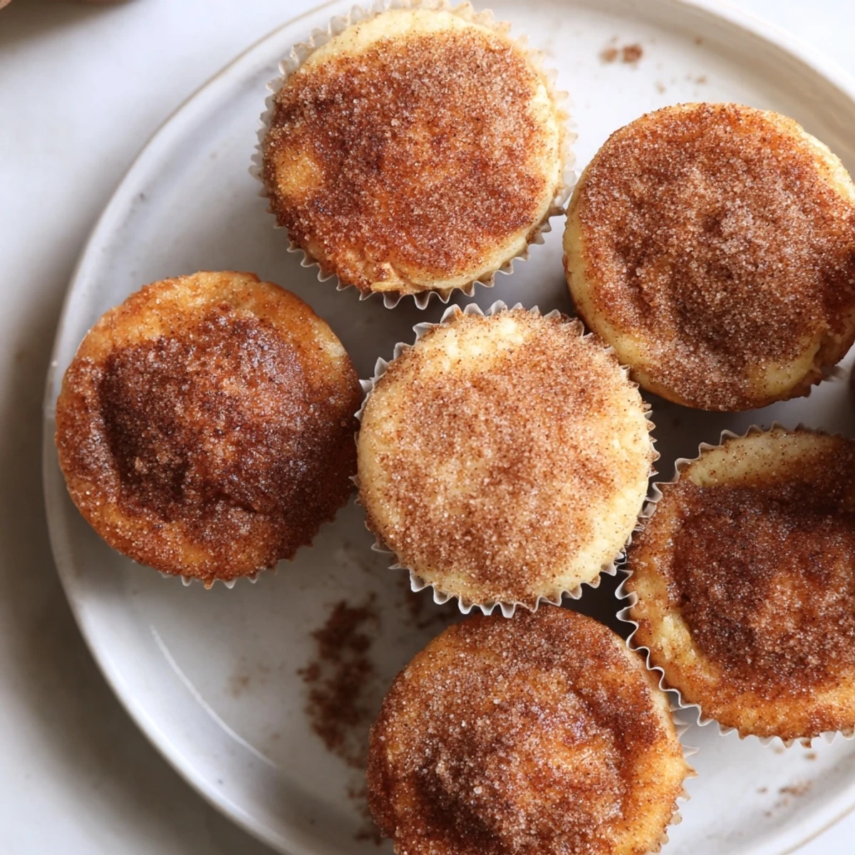 Twelve warm Cinnamon Sugar French Toast Muffins are arranged on a rustic platter, with a small pitcher of maple syrup nearby for dipping.  