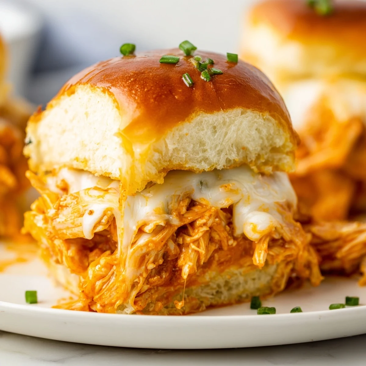 Warm Buffalo Chicken Pizza Dip Sliders baked golden brown with melted mozzarella and cheddar on fluffy Hawaiian rolls, garnished with fresh chives.