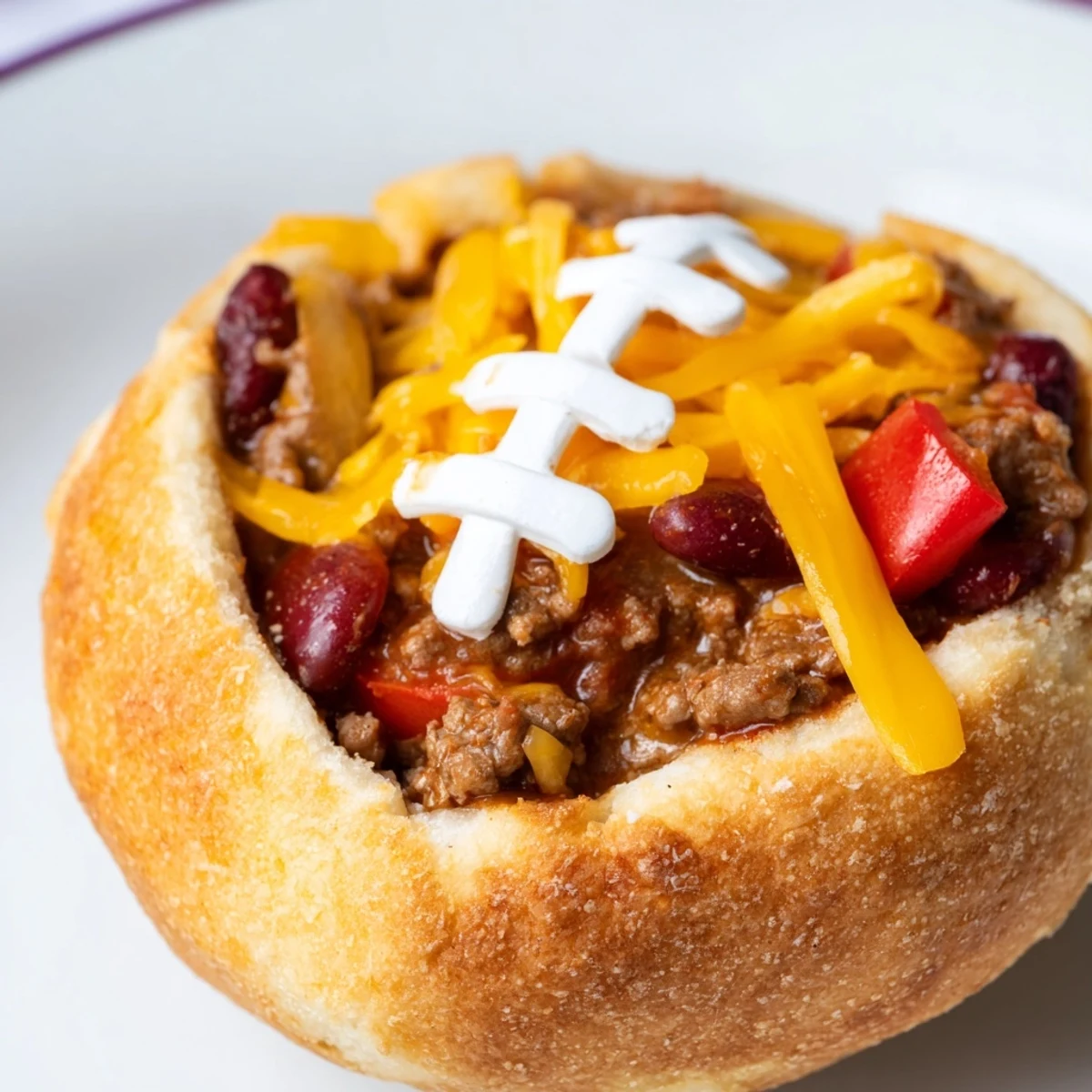 Mini Chili Football Bread Bowls with savory beef chili, gooey cheese, and fun sour cream detailing ready for a Super Bowl party.  