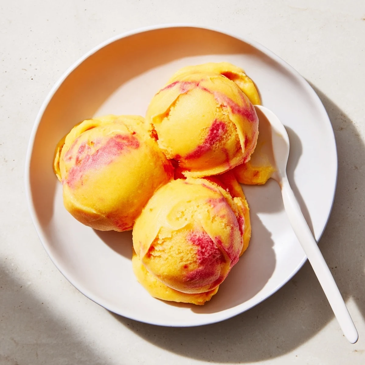 Bright scoops of Mango Strawberry Sorbet in a glass bowl, garnished with fresh mint for a refreshing summer treat.