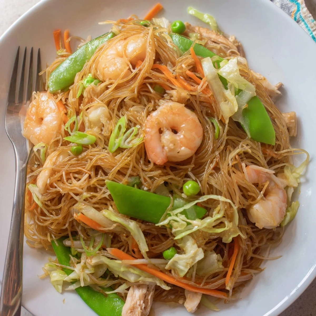 Golden bowl of traditional Pancit Bihon featuring tender rice noodles with chicken and crisp colorful vegetables