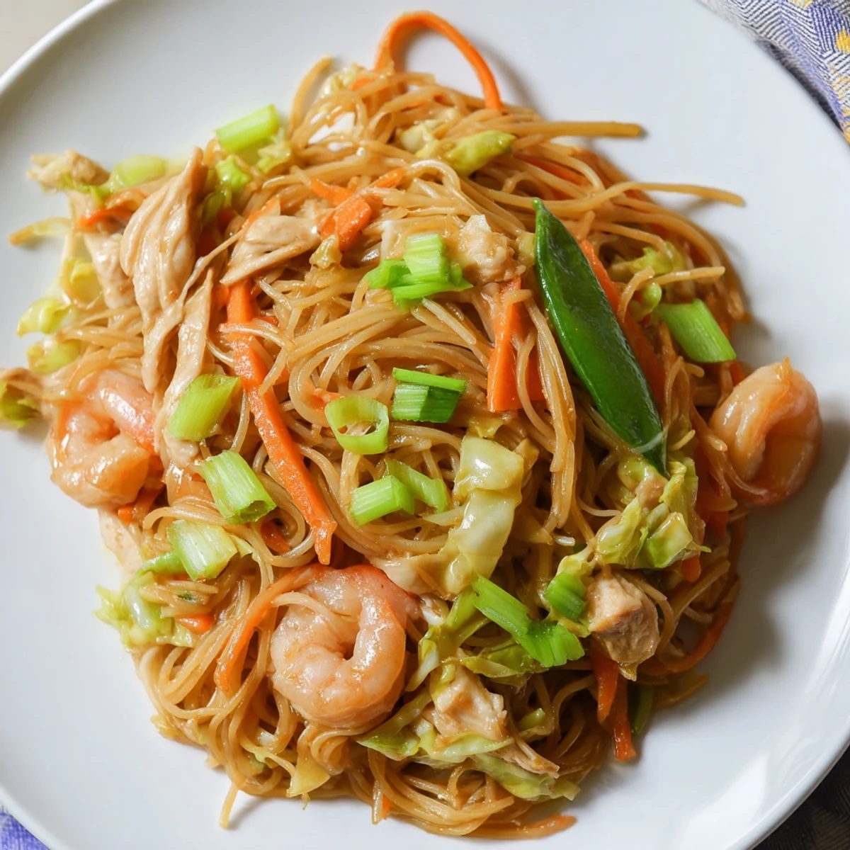 Steaming plate of traditional Pancit Bihon garnished with fresh scallions and lemon wedges for serving