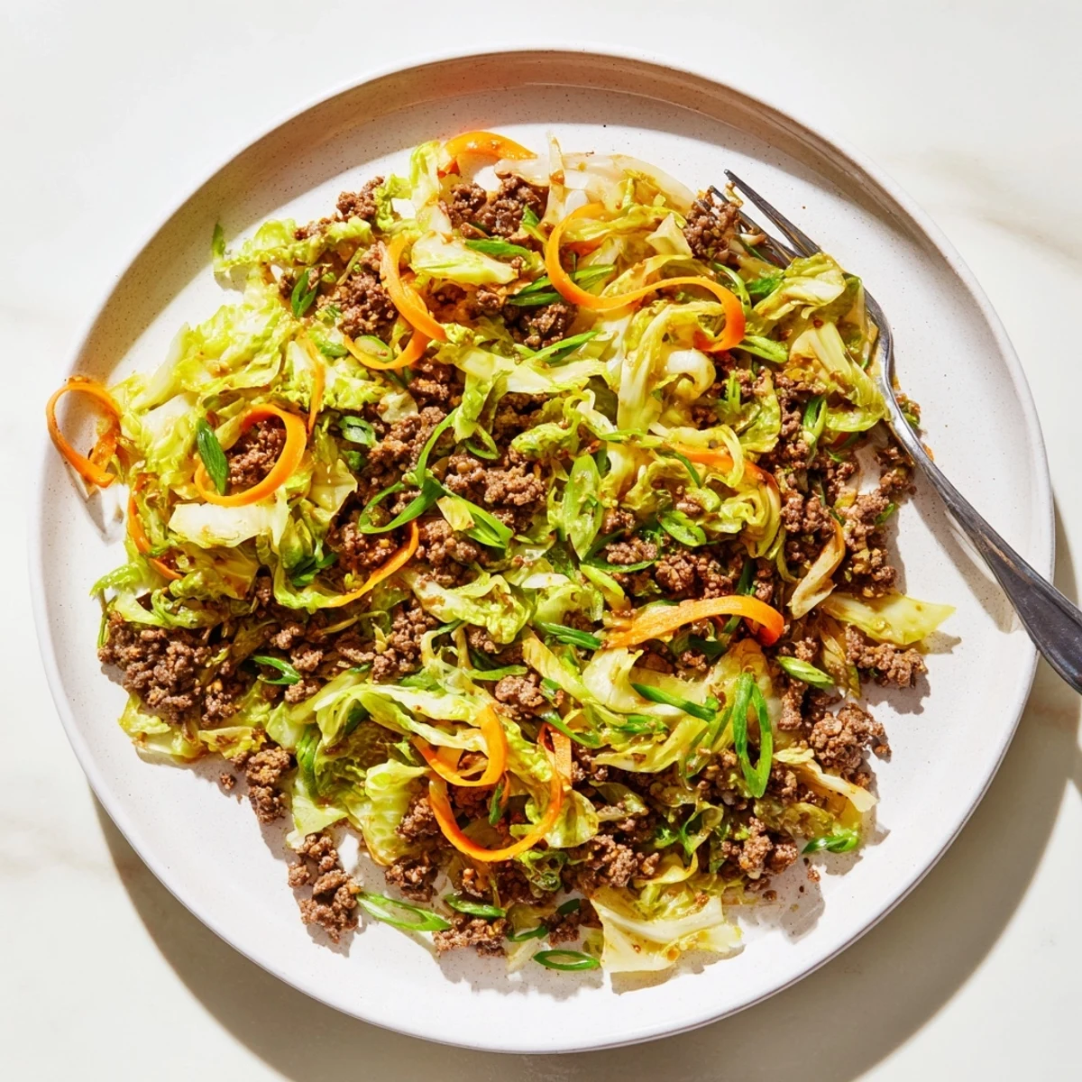 Golden brown ground beef and crisp green cabbage stir fry in a dark skillet garnished with fresh green onion slices