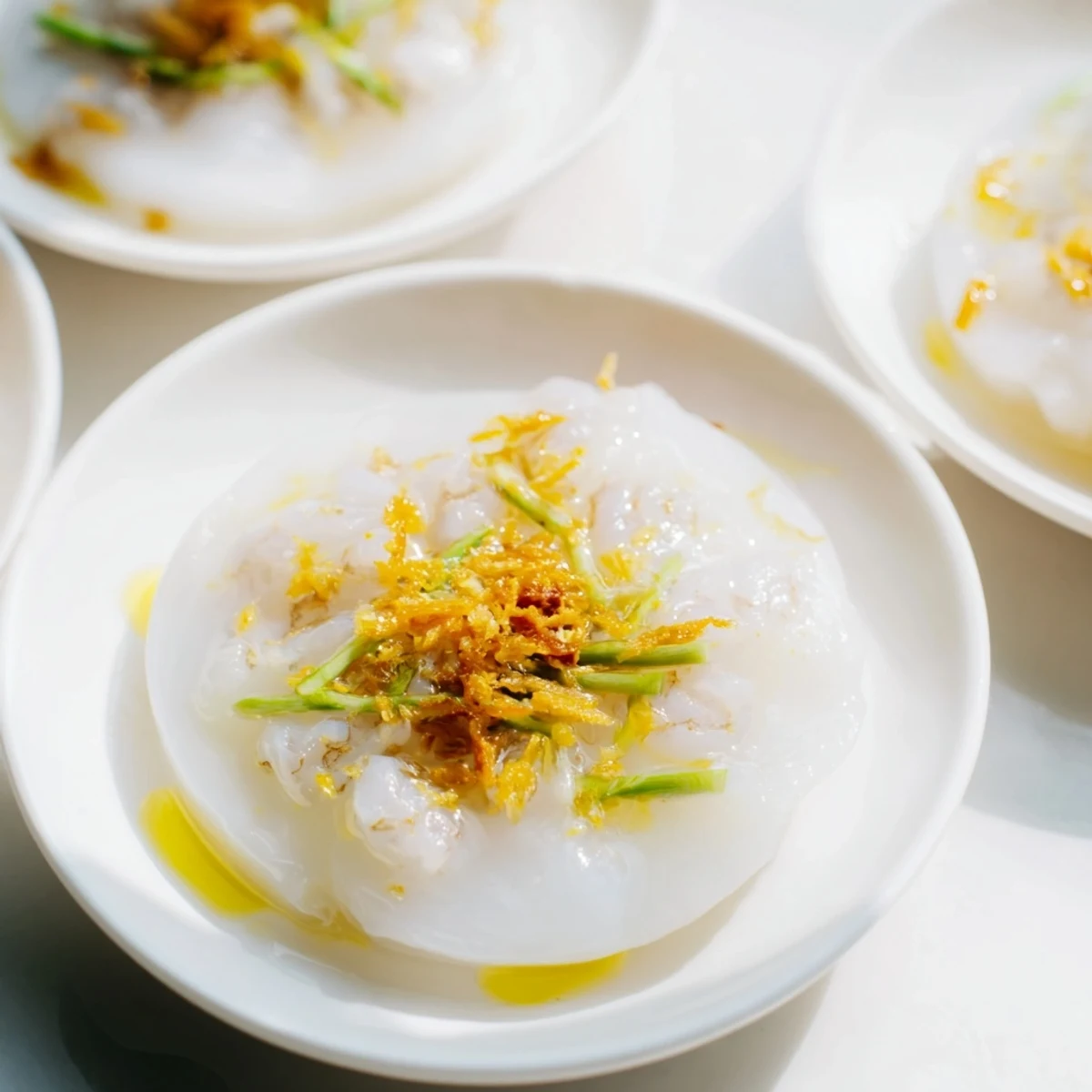 Steaming hot Banh Beo Vietnamese rice cakes topped with savory shrimp, scallion oil, and crispy shallots on small white plates