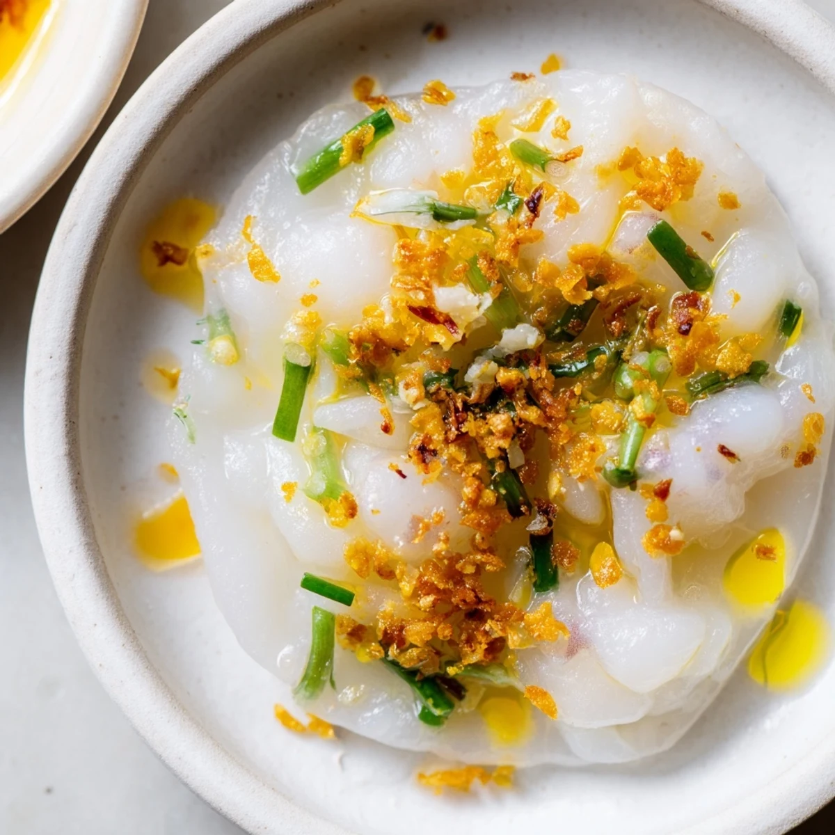 Delicate Banh Beo steamed rice cakes garnished with golden shrimp, vibrant scallion oil, and fried shallots ready for dipping