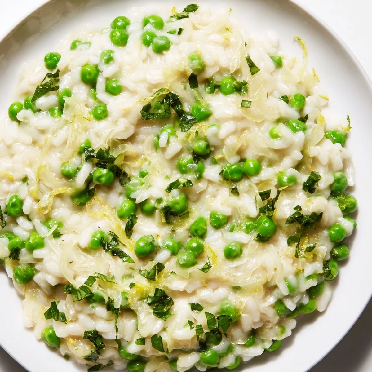 Steam rising from a bowl of spring pea risotto garnished with lemon zest and mint