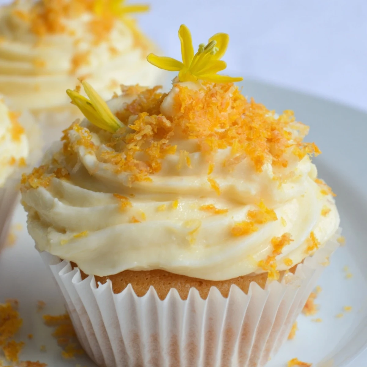 Golden orange blossom cupcakes with smooth buttercream frosting and decorative orange zest on white plate