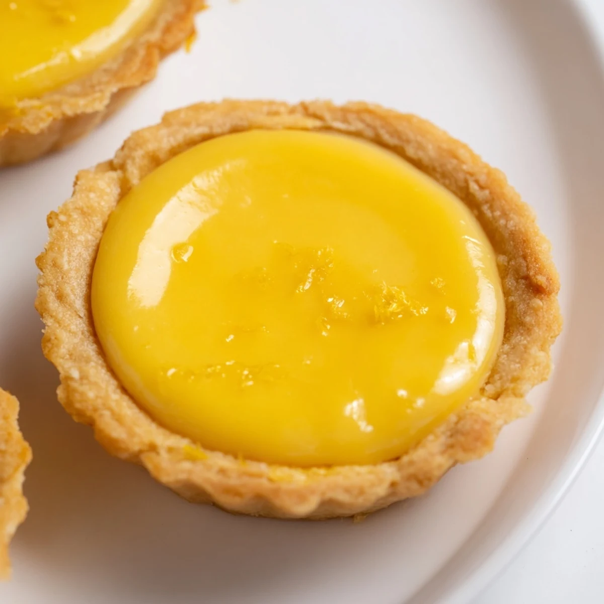 Bite-sized vegan lemon tarts topped with fresh lemon zest on a white serving plate