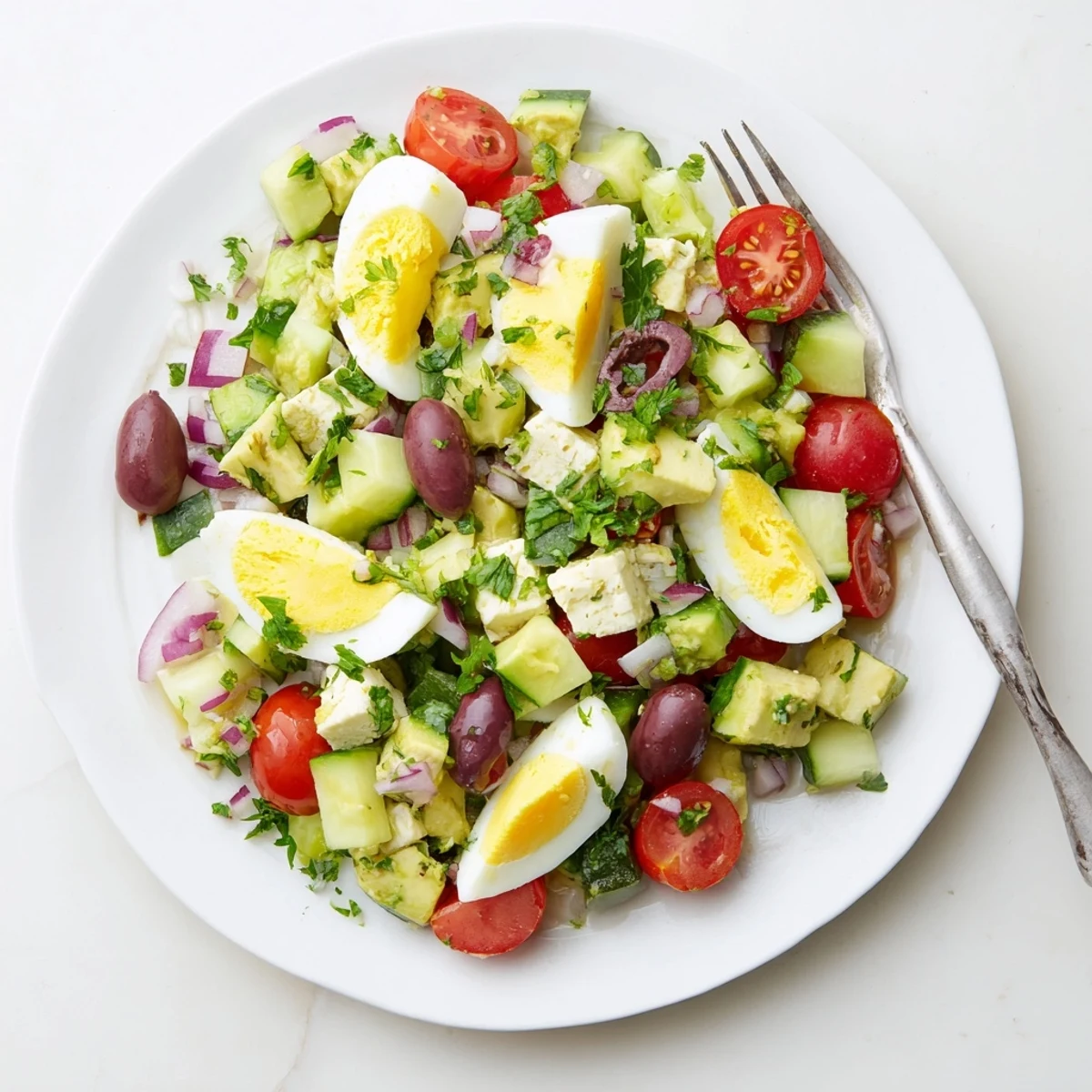 Vibrant bowl of Mediterranean avocado egg salad featuring cherry tomatoes, olives, and crisp cucumber