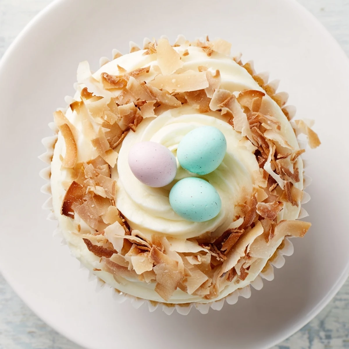 Golden coconut nest cupcakes topped with fluffy white frosting and colorful mini chocolate eggs arranged in a toasted coconut nest