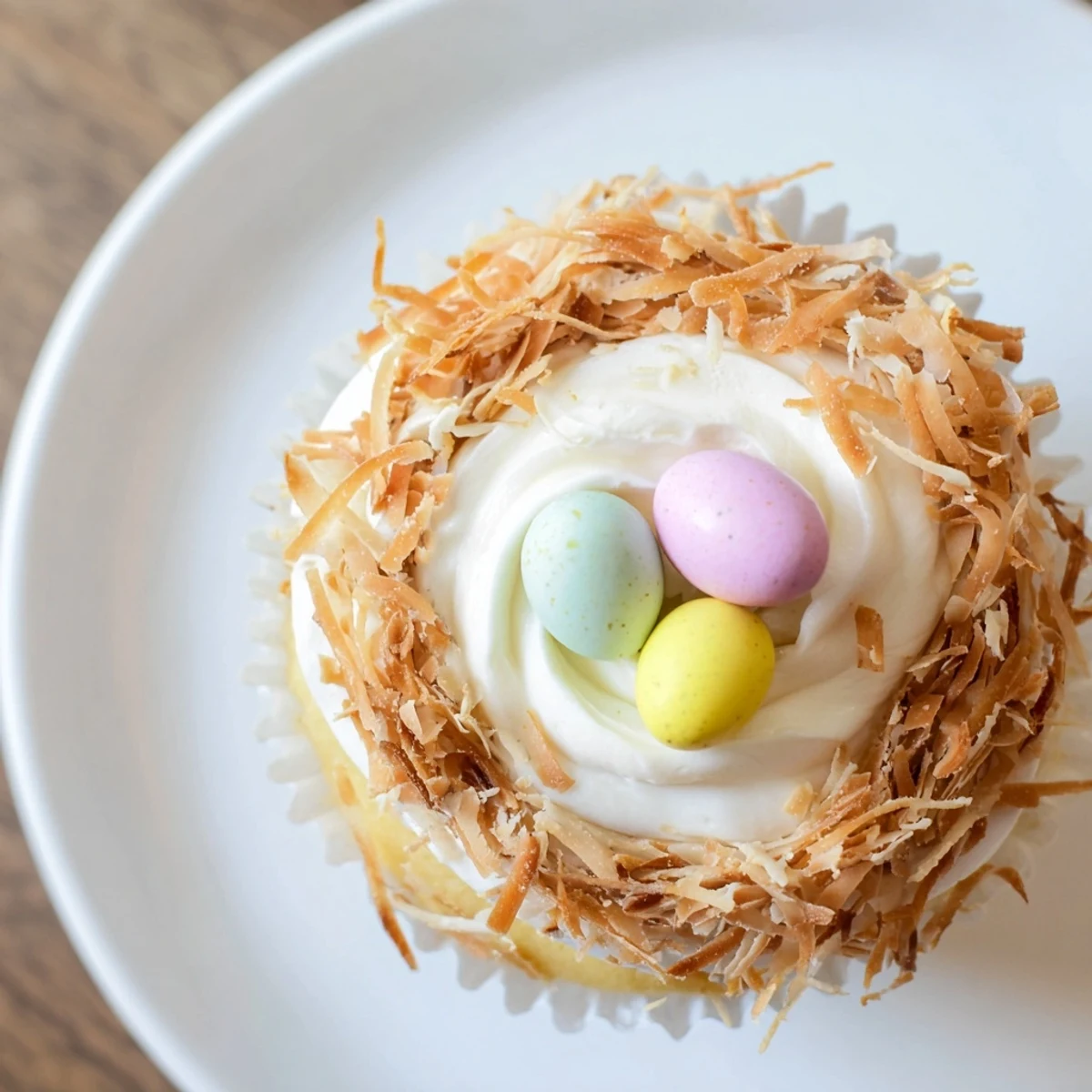 Coconut nest cupcakes displaying fluffy white frosting rings topped with golden toasted coconut and three chocolate eggs per cupcake