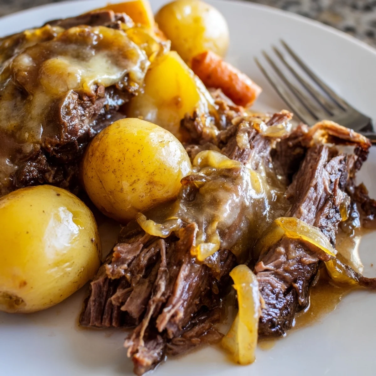 Tender French onion pot roast with caramelized onions, carrots, and baby potatoes in rich gravy