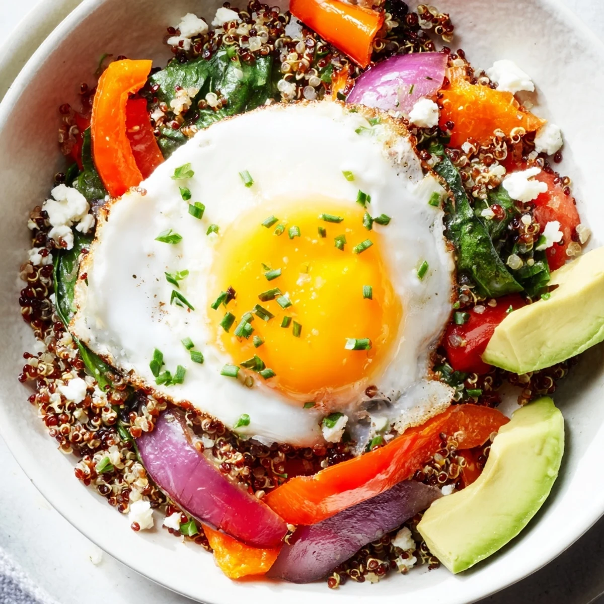 Protein-rich savory quinoa breakfast bowl featuring wilted spinach, cherry tomatoes, and runny egg