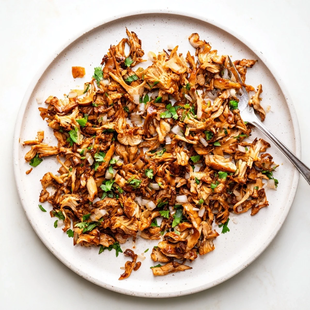 Golden brown vegan carnitas with shredded mushrooms nestled in warm corn tortillas topped with fresh cilantro and diced red onion