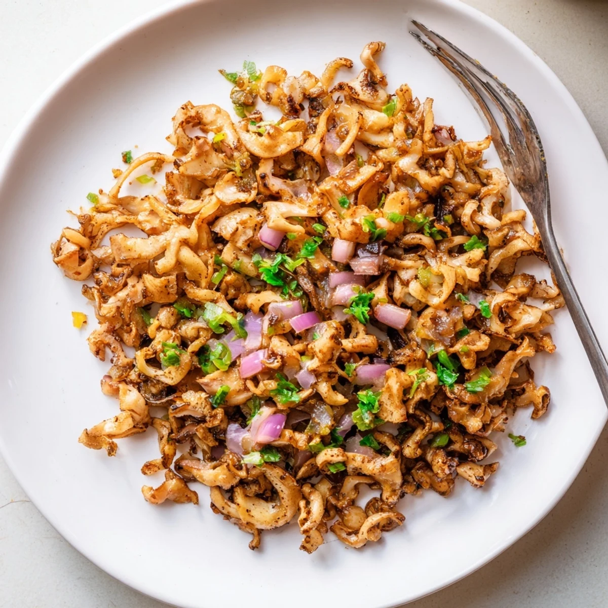 Crispy spiced mushroom carnitas arranged on a white platter with lime wedges, creamy avocado slices, and vibrant green onions