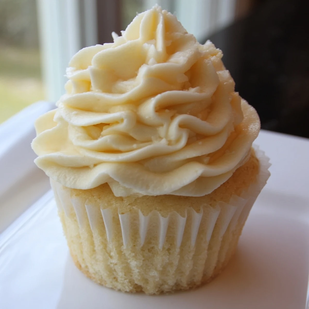 Golden vanilla cupcakes topped with creamy buttercream frosting on a rustic wooden serving board