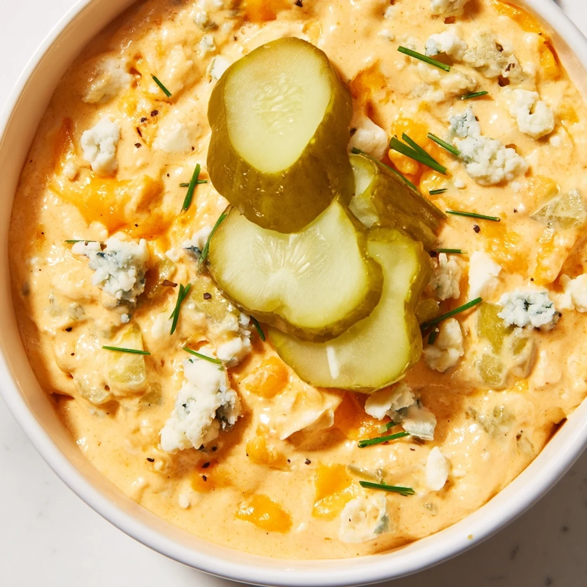 Tangy buffalo pickle dip topped with cheddar cheese and fresh chives in a rustic bowl