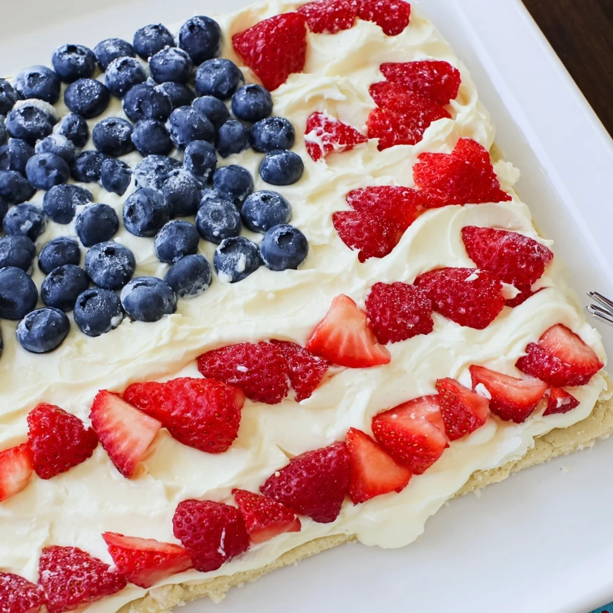 Creamy frosting topped with berries on Sugar Cookie Flag Fruit Pizza, chilled.