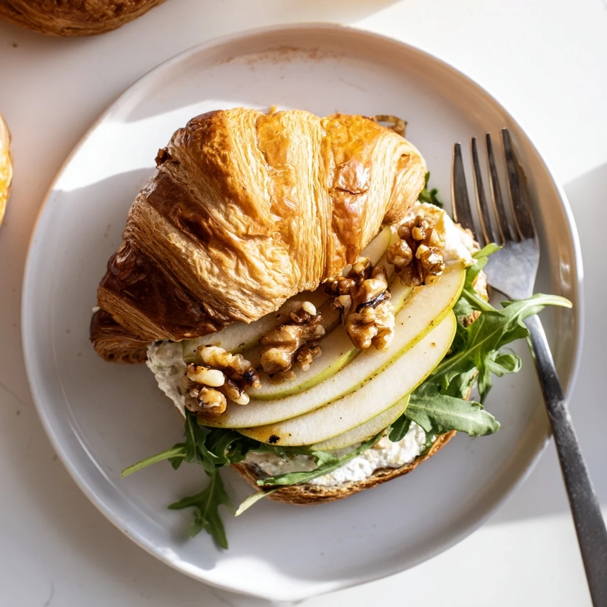 Apple Goat Cheese Croissant Sandwich served open-faced on wooden board, arugula peeking
