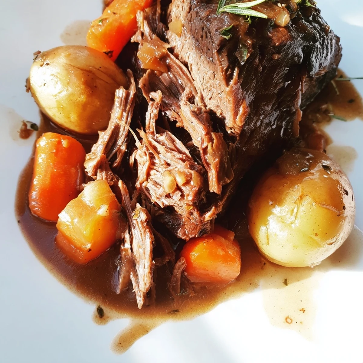 Golden brown herb braised beef chuck roast plated with baby potatoes and fresh thyme sprigs