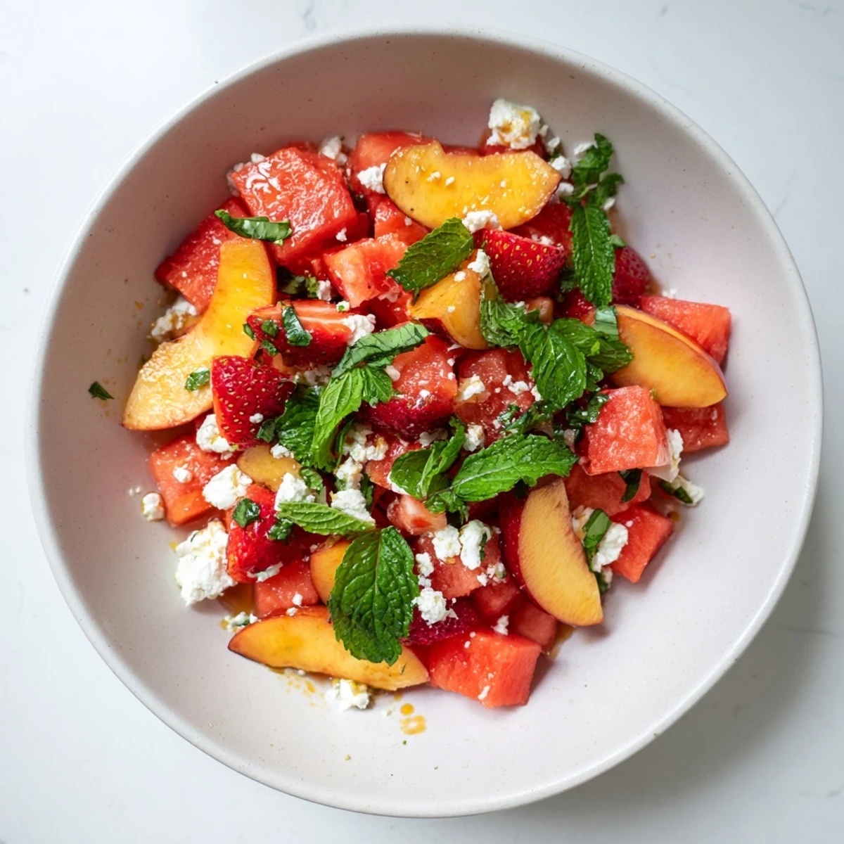 Bowl of refreshing Summer Peach Watermelon Salad garnished with crumbled feta cheese and torn mint leaves