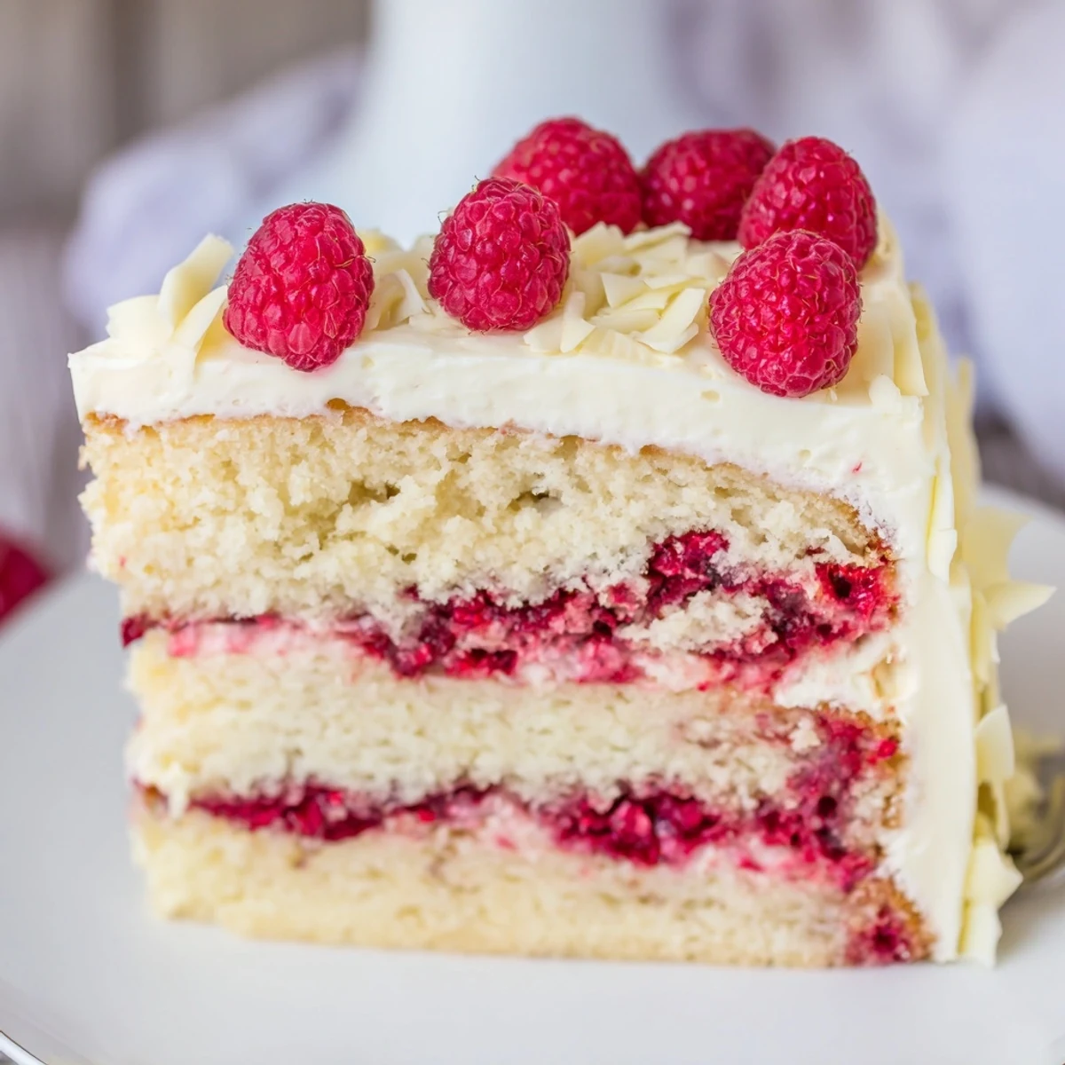 Slice of white chocolate raspberry dream cake showcasing swirled raspberry jam filling and fluffy cream cheese white chocolate frosting on a dessert plate