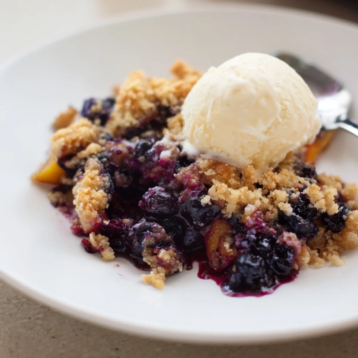 Warm Blueberry Peach Crumble bubbling in a golden dish, topped with ice cream