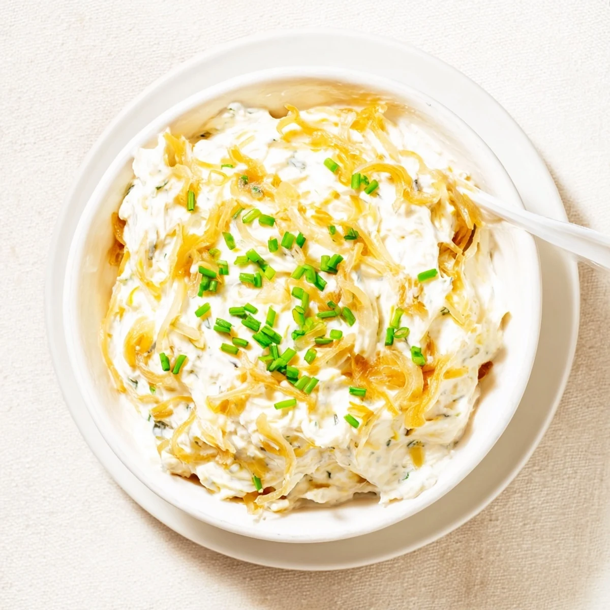 Rich French onion dip served in a white bowl surrounded by potato chips and vegetable crudités