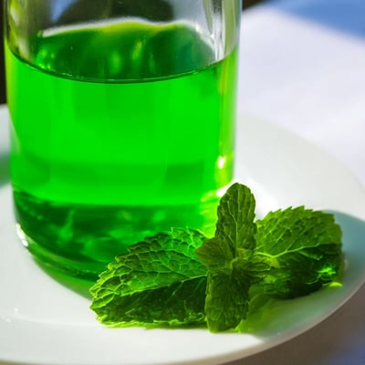 A small bottle of homemade peppermint extract beside fresh leaves and a gift tag.