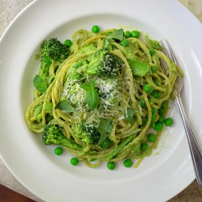 A bowl of creamy Veggie Smuggler Avocado Pasta with steamed broccoli and peas.